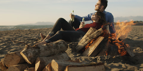 Image showing Loving Young Couple Sitting On The Beach beside Campfire drinkin