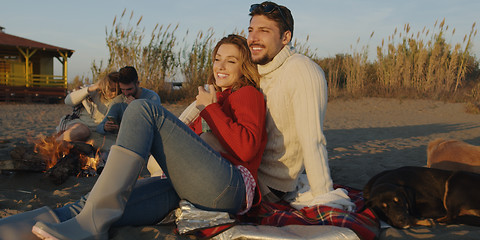 Image showing Loving Young Couple Sitting On The Beach beside Campfire drinkin