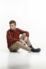 Image showing Casual young man sitting on the floor and looking to a side, away from the camera, on a white background