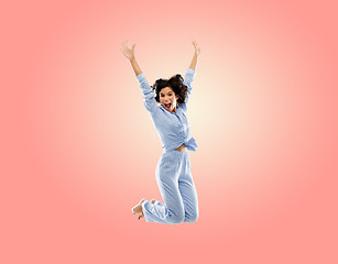 Image showing happy woman in blue pajama jumping high over pink