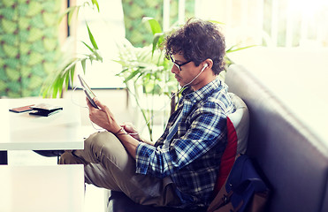 Image showing man with tablet pc and earphones sitting at cafe