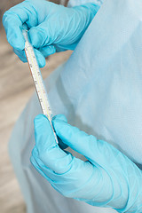 Image showing Hands of medic in sterile gown and gloves hold thermometer