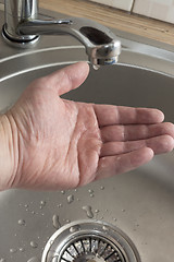 Image showing A drop of water drips in mans palm who checks if there is water in kitchen tap