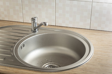 Image showing Clean round metal kitchen sink with faucet and water drops from leak