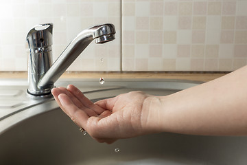 Image showing A drop of water drips from faucet in human palm above round metal kitchen sink