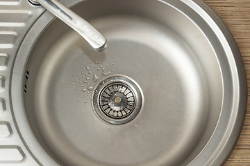 Image showing Drops on the bottom of clean round metal kitchen sink with a leaking tap