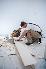 Image showing Man cutting laminate floor plank with electrical circular saw