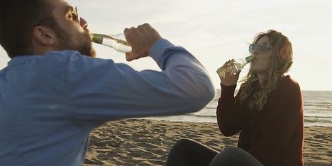 Image showing Loving Young Couple Sitting On The Beach beside Campfire drinkin