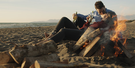 Image showing Loving Young Couple Sitting On The Beach beside Campfire drinkin