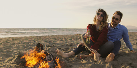 Image showing Loving Young Couple Sitting On The Beach beside Campfire drinkin