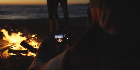 Image showing Couple taking photos beside campfire on beach