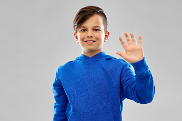 Image showing smiling boy in blue hoodie waving hand