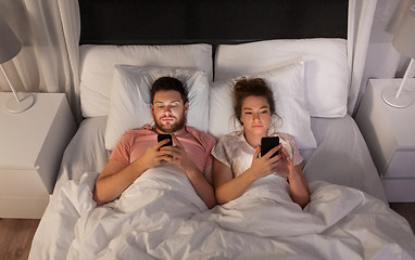 Image showing couple using smartphones in bed at night