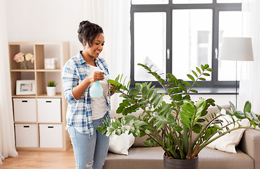 Image showing happy african woman spraying houseplants at home