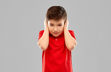 Image showing stressed boy in red t-shirt closing ears by hands