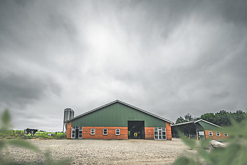 Image showing Cow standing by a red barn in a rural countryside