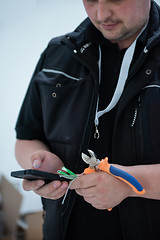 Image showing electrical engineer with wire and pliers in his hand using mobil