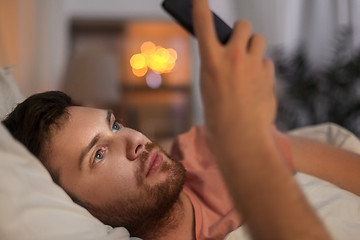 Image showing young man with smartphone in bed at night