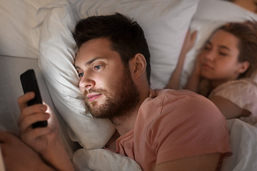 Image showing man using smartphone while girlfriend is sleeping