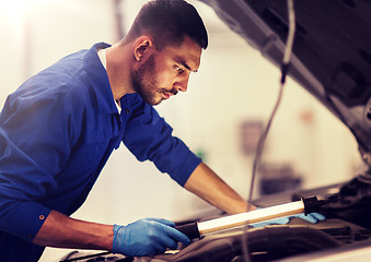 Image showing mechanic man with lamp repairing car at workshop