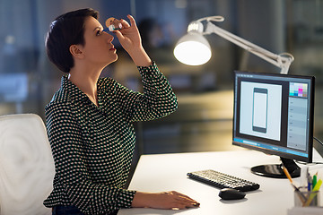 Image showing female designer using eye drops at night office