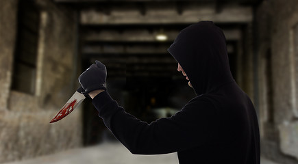 Image showing criminal with bloody knife over dark gateway