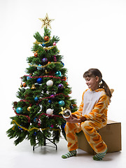 Image showing Teenage girl sits on a box at a Christmas tree and examines a Christmas tree