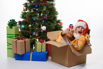 Image showing The girl sits in a box of Christmas trees near the Christmas tree and cheerfully looks into the frame