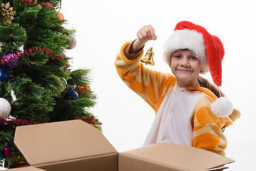 Image showing The girl took out a toy bell out of the box and is going to hang it on the Christmas tree