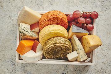 Image showing Fresh and delicious different kinds of cheeses placed in wooden crate with grapes