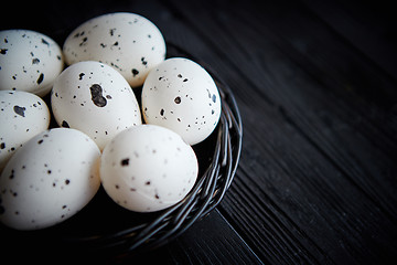 Image showing Whole Chicken eggs in a nest on a black rustic wooden background. Easter symbols