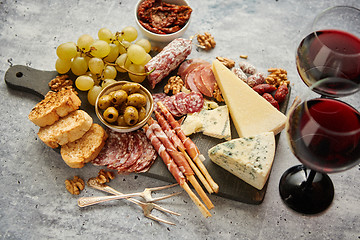 Image showing Cold snacks board with meats, grapes, wine, various kinds of cheese