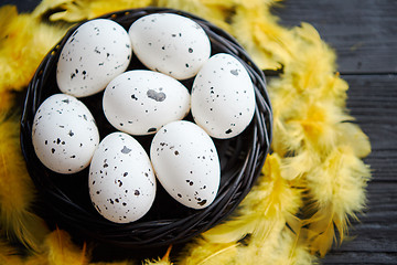 Image showing Whole Chicken eggs in a nest on a black rustic wooden background. Easter symbols