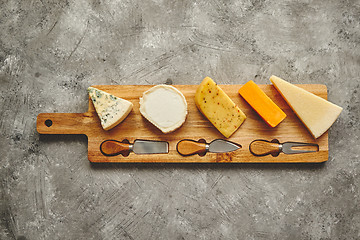 Image showing Assortment of various kinds of cheeses served on wooden board with fork and knives