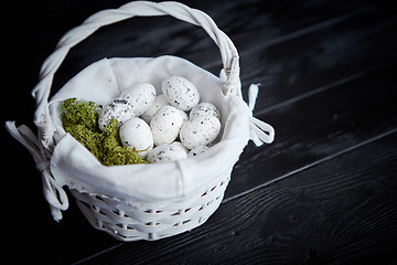 Image showing Quail eggs in a nest on a black rustic wooden background. Easter symbols