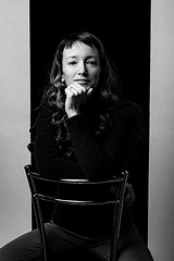 Image showing Cute girl sits on a bar chair and clouds her hands on the back of a chair, black and white photo