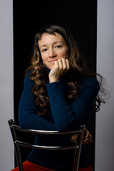 Image showing Cute girl sits on a bar chair and clouds her hands on the back of a chair, black gray background