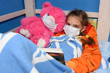 Image showing Girl and plush toy in medical masks in bed read a book, and looked into the frame