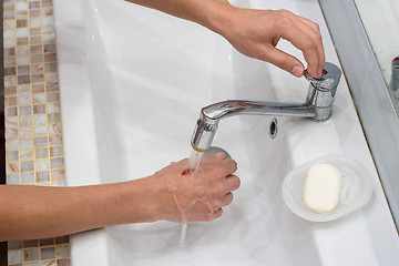 Image showing A man washes a wound on his hand under a stream of water in the washbasin