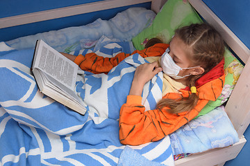 Image showing The sick girl went to bed to read a book and for a while removed the medical mask