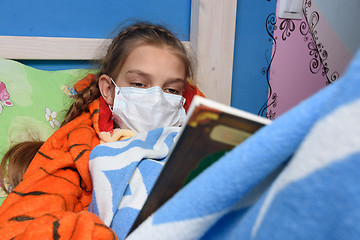 Image showing Teenage girl lies in medical mask in bed and reads book