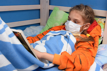 Image showing Sick girl in medical mask lies in bed and reads a book