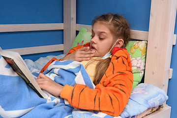 Image showing Sick girl sneezes lying in bed and reading a book