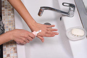 Image showing Girl applies cream on skin of hands in the bathroom