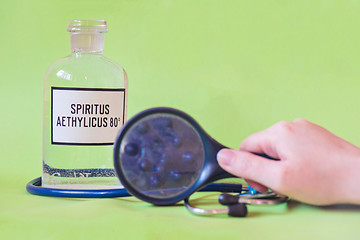 Image showing Ethanol in a bottle on the table with of microscope virus close up, stethoscope and loupe with fingers. Coronavirus concept