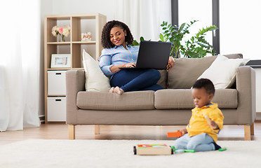 Image showing mother with laptop looking at baby with toy blocks