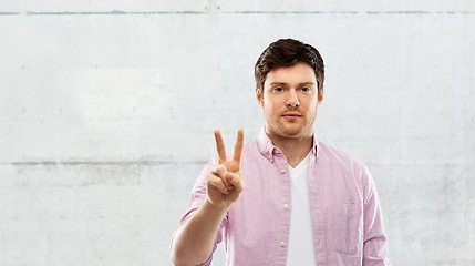 Image showing young man showing two fingers over grey background