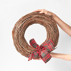 Image showing Woman\'s hands hold round wreath from dry twigs with bow.