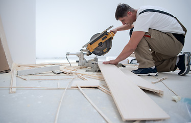 Image showing Man cutting laminate floor plank with electrical circular saw