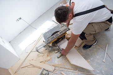 Image showing Man cutting laminate floor plank with electrical circular saw